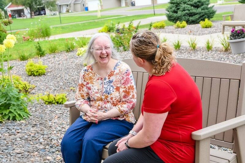 Photo of a woman laughing on bench outside with senior living nurse