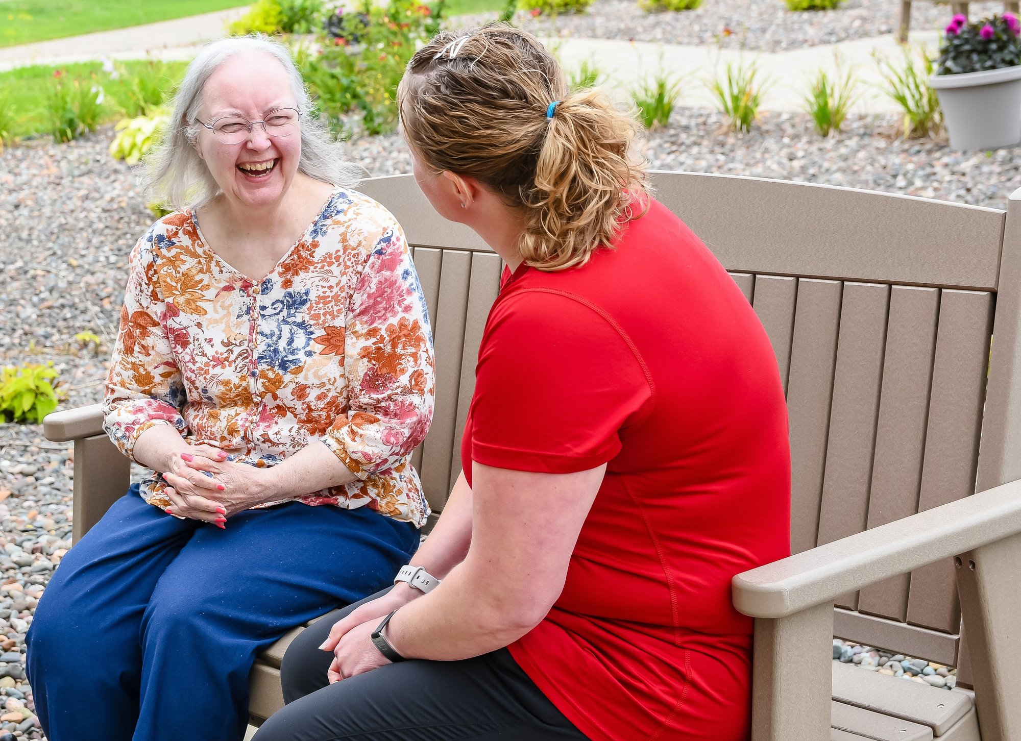 Photo of a woman laughing on bench with senior living nurse