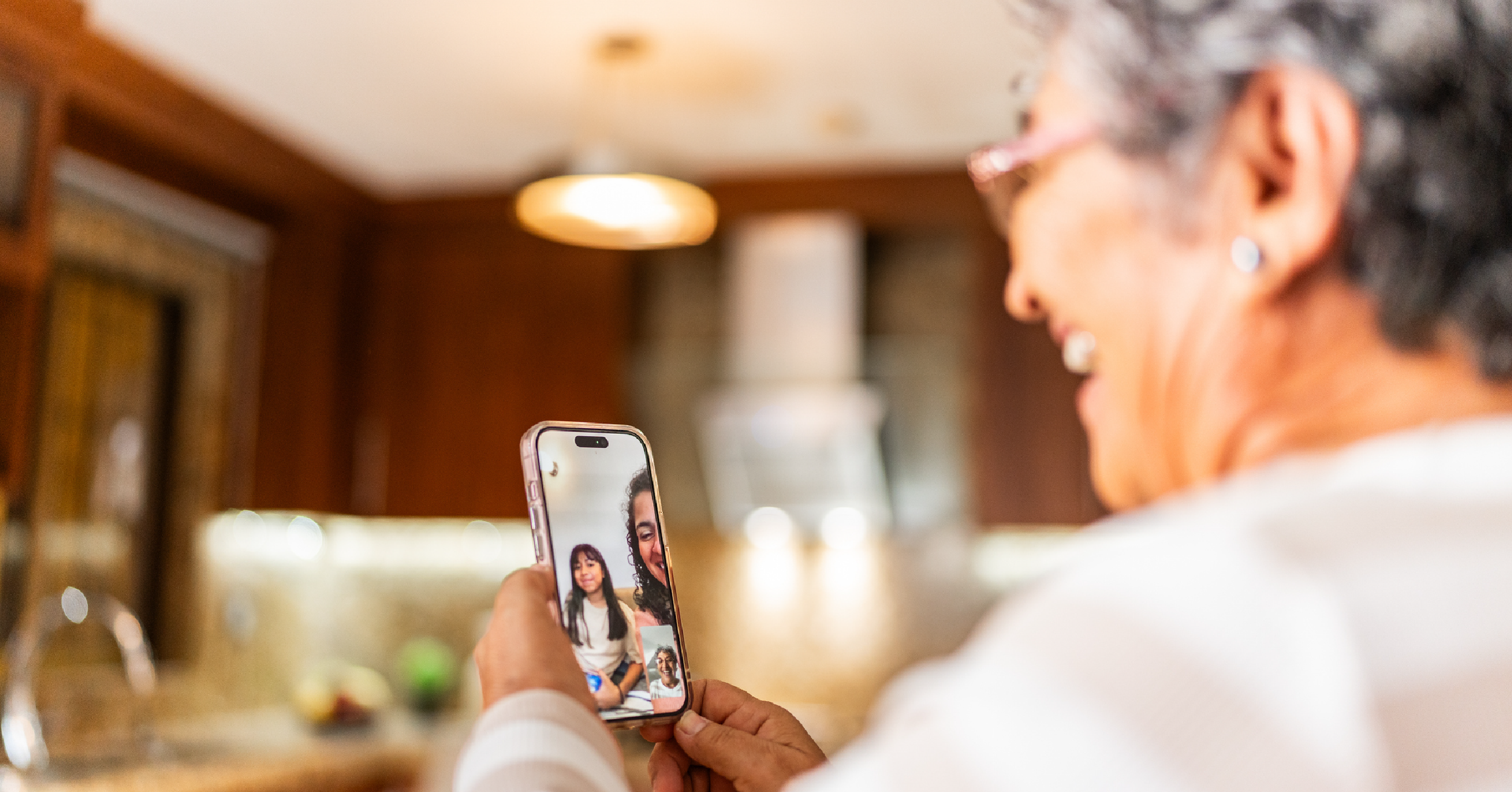 An older woman holds a mobile phone showing a video conversation with a younger person.
