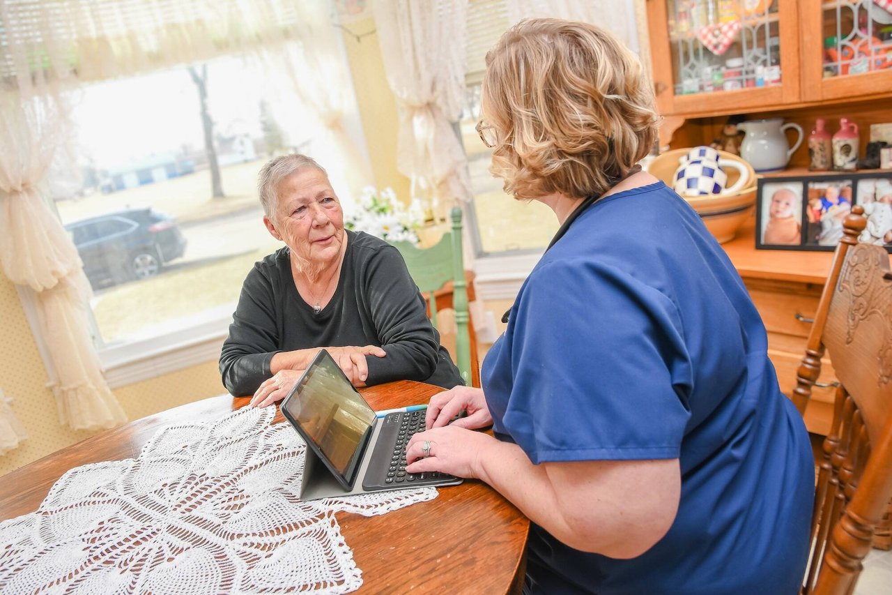 nurse with computer talking with senior woman at dining room table