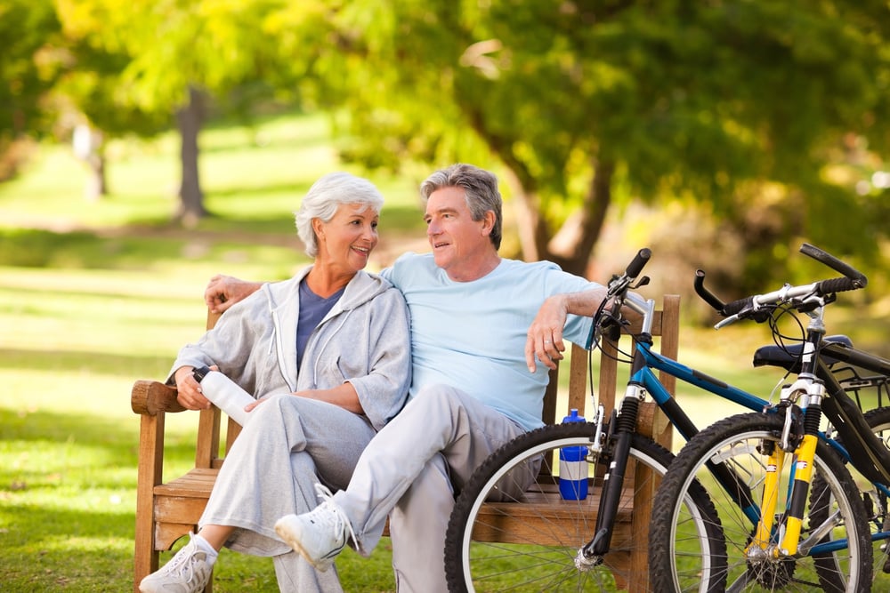 Photo of an older couple with their bikes taking a break on a park bench