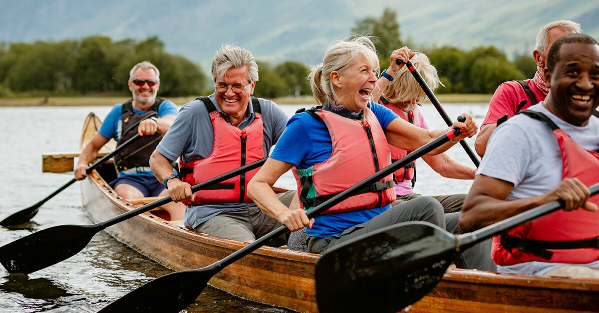 Senior in lifejackets paddle in canoe on lake