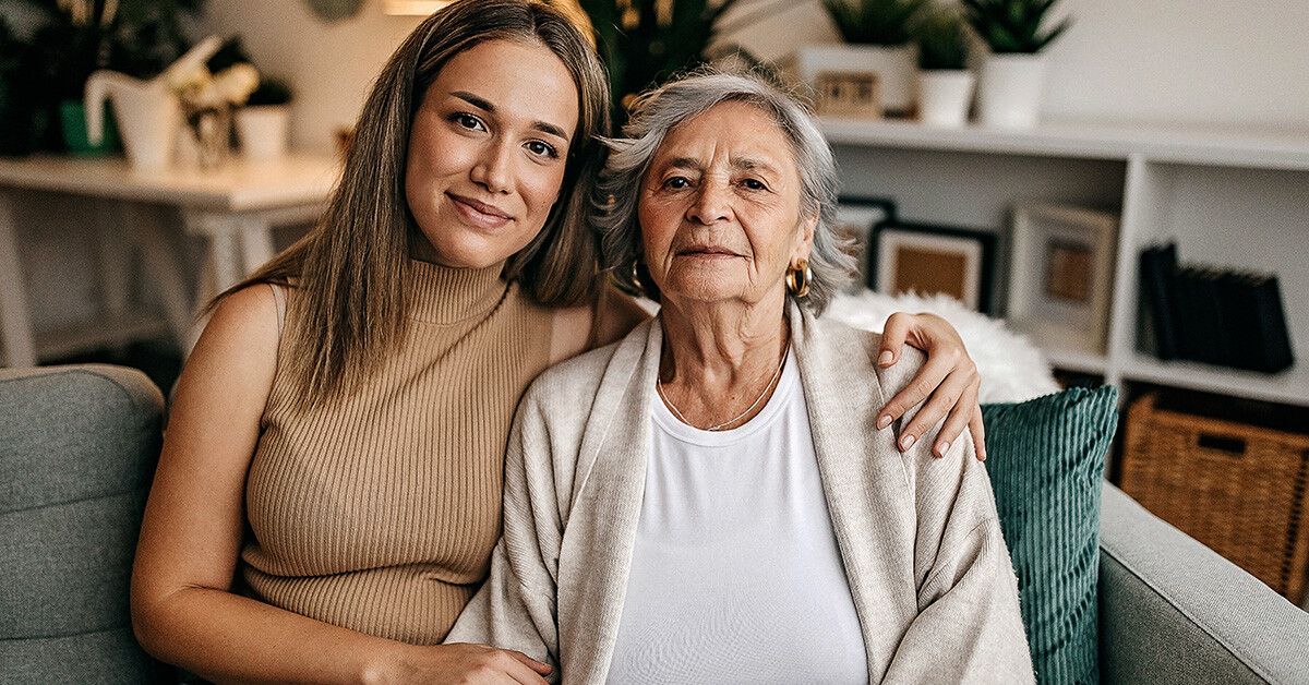 Senior woman and daughter sit on couch looking at camera-3