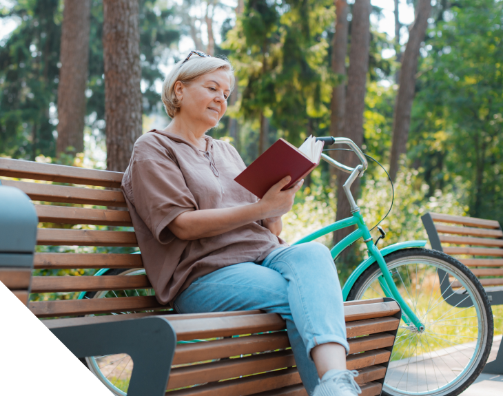 Photo of woman reading book on bench outside with bicycle