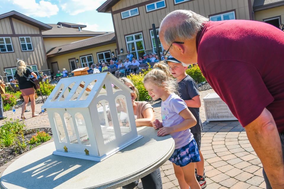 older man looking into small white house with children