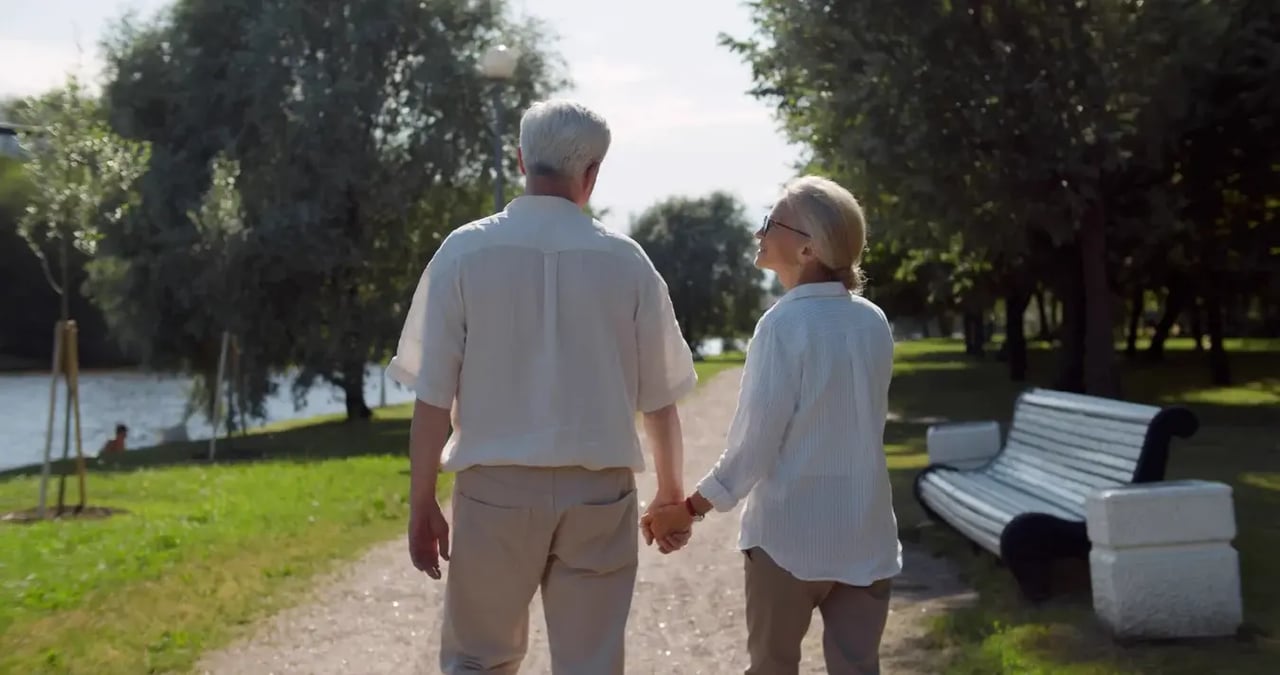 white-haired couple holding hands on walking path outdoors