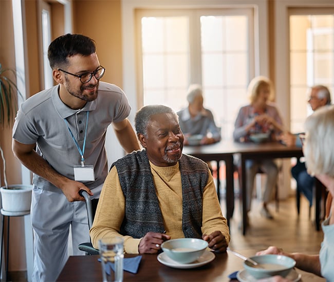 nurse helping older man in full dining room