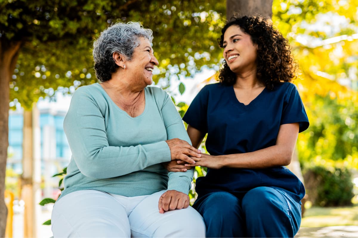 n-older-woman-and-a-younger-female-caregiver-sitting-together-outdoors-smiling-and-holding-hands