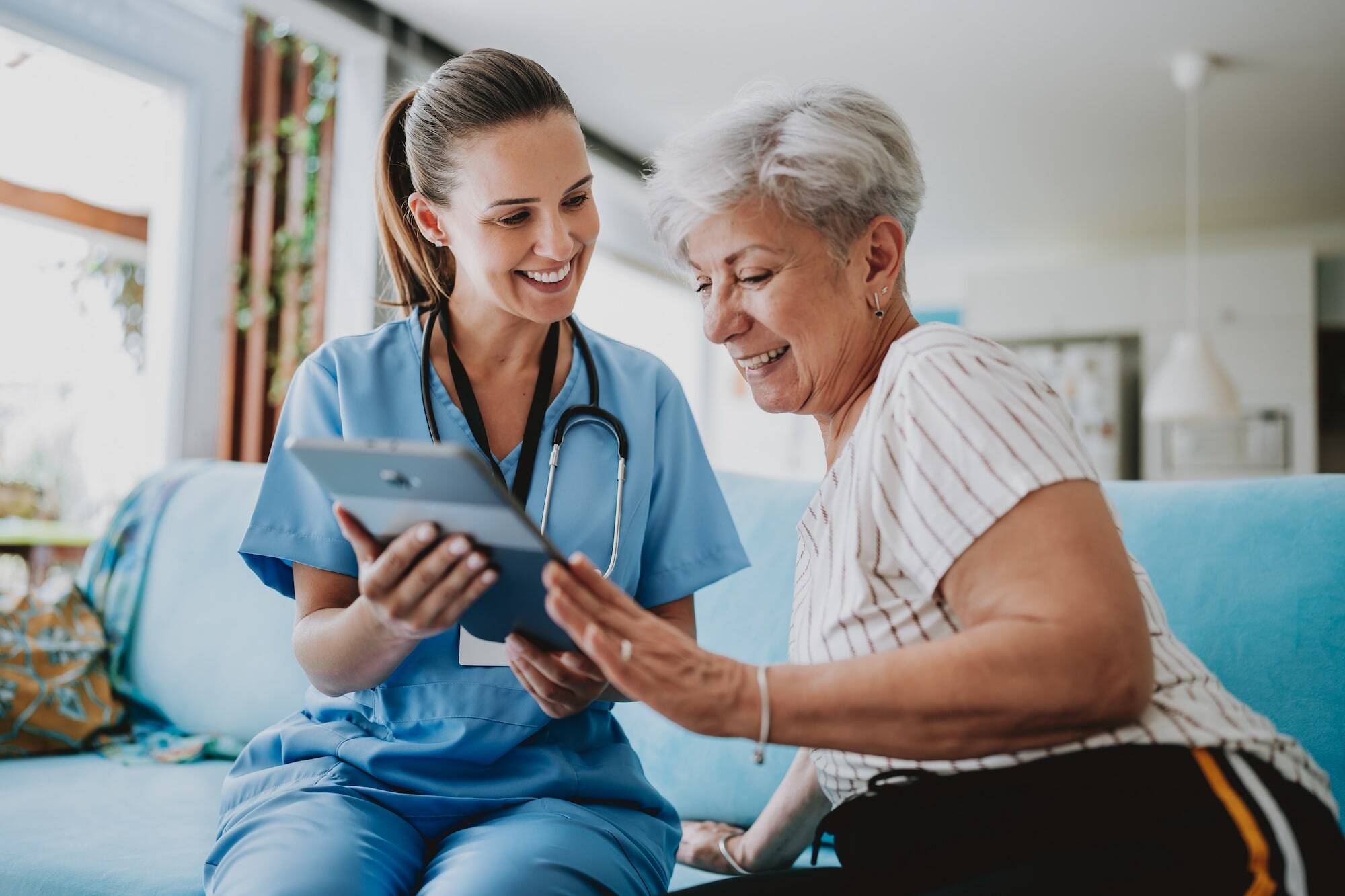 Photo of a home healthcare nurse showing tablet to older woman